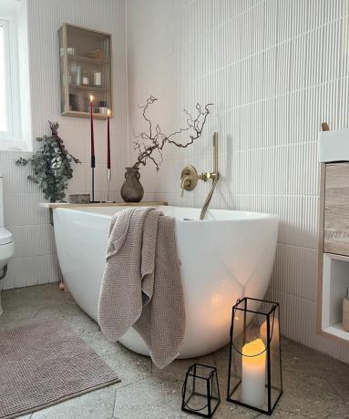 Bak mandi putih dengan handuk dan vas dengan cabang
