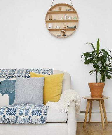 Dettaglio divano moderno con copriletto a quadri grigi, cuscini gialli e grigi in un soggiorno bianco