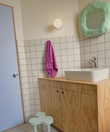 흰색 타일 벽, 녹색 파스텔톤 스툴과 거울, 보라색 문이 있는 욕실
