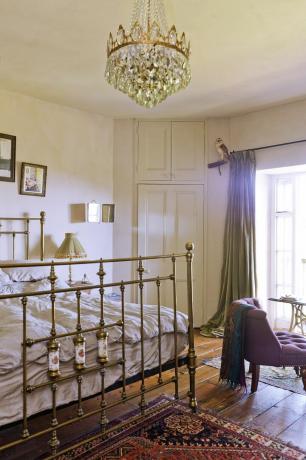 спаваћа соба са креветом од ливеног гвожђа и украшеним светлим перзијским тепихом и дрвеним подовима