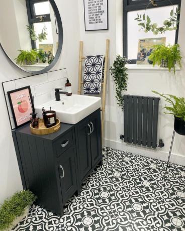 Ванная комната с черной раковиной, зеркалом, радиатором и растениями.