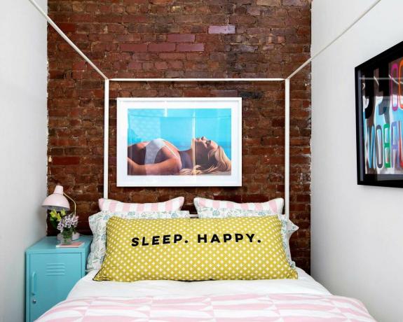 むき出しのレンガの壁と白い四柱式ベッドのあるニューヨークのアパートの小さなベッドルーム