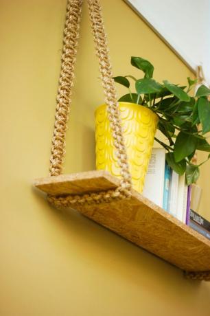 Scaffale con appendiabiti in corda dorata e vaso per piante giallo contro il muro giallo