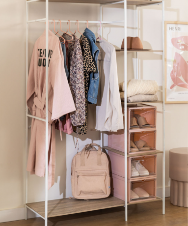 Белая вешалка для одежды с местом для хранения розовых обувных коробок и набором нейтральной и джинсовой одежды.