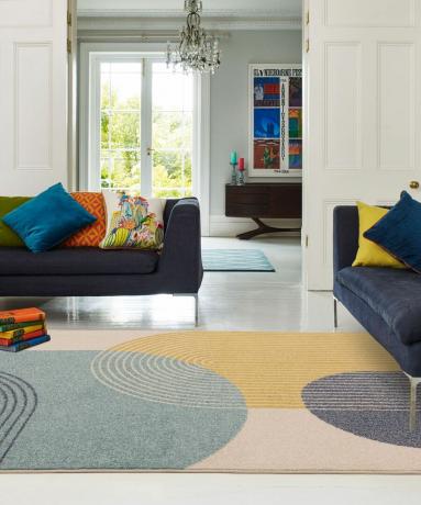 Kraftige geometriske tepper i stor skala med blå sofaer med flerfargede puter.