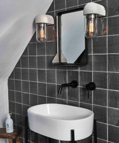 Rivestimenti grigi con applique trasparenti, lavabo bianco e rubinetti neri