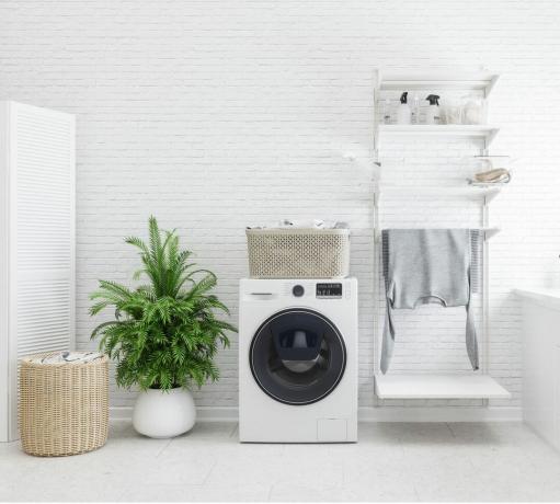 wasruimte-ideeën - een witte wasmachine in een wit betegelde wasruimte - GettyImages-1188826574