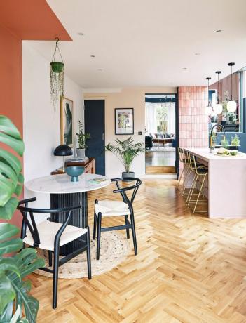 Köök-söögituba roosade seinte, parkettpõranda, roosa köögisaare ning musta ja marmorist laua ja toolidega