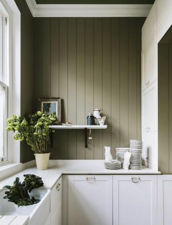 Een kleine saliegroene keuken met marmeren aanrecht, witte kasten, open planken en wandpanelen
