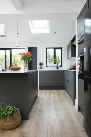 Melnas virtuves iekārtas, balta darba virsma un koka efekta lamināta grīda