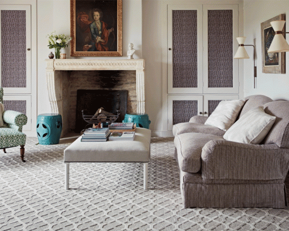 En traditionel stue med tekstureret lysegråt tæppe, lysegrå sofa og creme kaminhylde