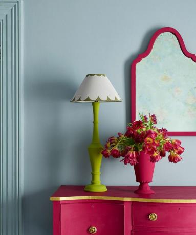 파란색 벽에 핑크색 거울과 옷장이 있고 꽃과 램프가 있음