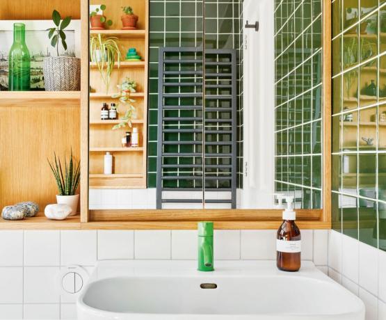 Aufnahme eines Waschbeckens mit grünem Wasserhahn, Spiegel und eingebautem Eichenregal, weißen quadratischen Rückwandfliesen und tiefgrünen Wandfliesen
