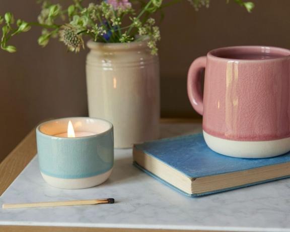 bougie dans un pot bleu par une tasse, un livre et un vase roses