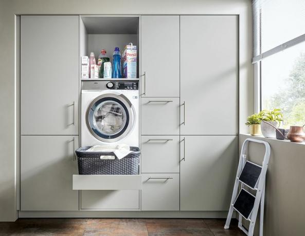Un lavadero con taburete, unidades integradas de color gris pálido integradas con unidad extraíble para lavadora, cesto de ropa y detergente para ropa