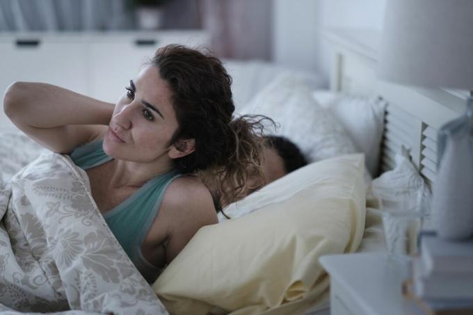 En kvinne i en seng som sliter med å sove ved siden av sovende partner