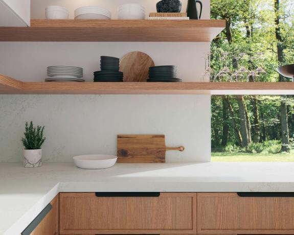 Una cucina con piano di lavoro in quarzo bianco, ripiani in legno e stoviglie assortite su scaffalature