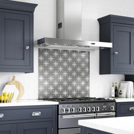 Η Laura Ashley μοτίβα μονόχρωμη πλάτη πάνω από την κουζίνα σε μια σκούρα μπλε κουζίνα με ντουλάπια shaker