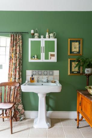 zaļa vannas istaba ar baltu izlietni un spoguli
