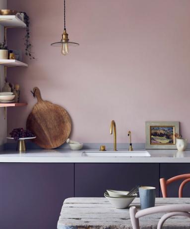 Toninės violetinės spalvos virtuvė su kontrastingos spalvos sienele ir spintele