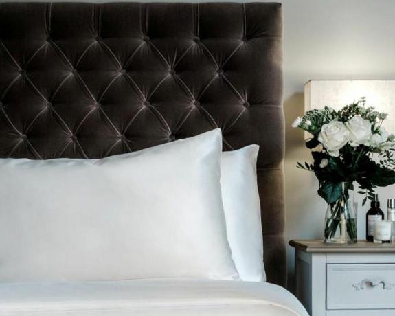 Um conjunto de duas almofadas envoltas em fronhas de seda na cama com botão de veludo na cabeceira da cama