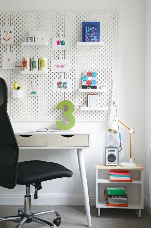 Colț al unui birou de acasă cu birou alb, panou alb și scaun negru de birou
