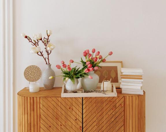 Dekoro aksesuarai šiuolaikiškos šviesios svetainės su baltomis sienomis ir mediniais baldais interjere. Šviežių rožinių tulpių gėlių puokštė.