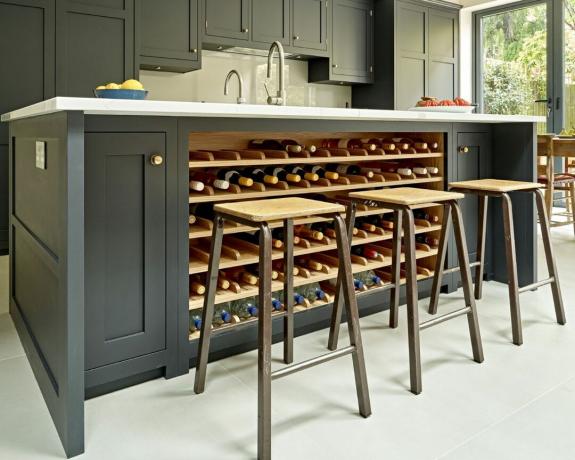 Tamsi virtuvės sala su integruota vyno saugykla ir pramoninio stiliaus baro kėdėmis