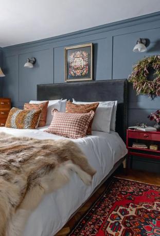 Camera da letto con pareti rivestite in blu, testata del letto in pelle e tappeto a fantasia rossa