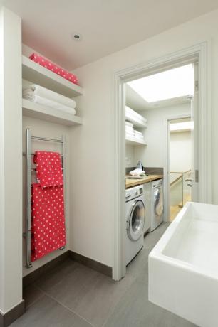 Una lavanderia/ripostiglio con piano di lavoro in legno, lavatrice, asciugatrice e scaffali aperti all'interno di un bagno