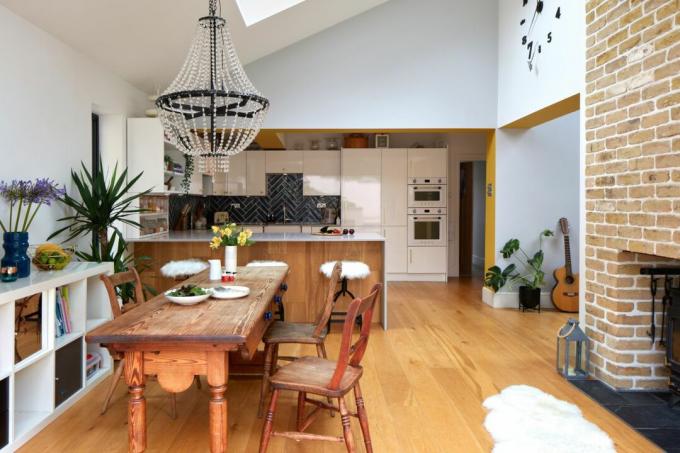 Razširjen prostor z belimi stenami, lesenim podom, lesom in belo kuhinjo, rustikalno leseno jedilno garnituro z lestencem iz perl nad glavo