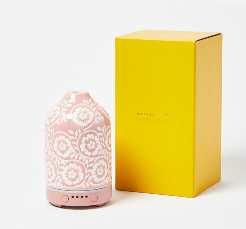 Un difuzor de ulei esențial roz lângă o cutie galbenă pe fundal alb.