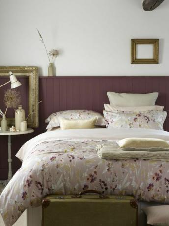 Makuuhuone, jossa on maalatut violetit seinäpaneelit, kuviolliset liinavaatteet ja koristeelliset kehykset