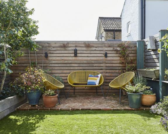Terrasse de jardin de style palette et clôture avec canapé d'extérieur jaune et chaises longues