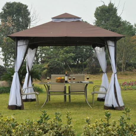 Un grand gazebo avec des rideaux et un dessus marron couvre la configuration des repas en plein air sur une pelouse de jardin