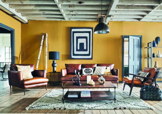 sala de estar amarilla con obras de arte en blanco y negro, sofá y sillones de cuero, mesa de centro de madera y alfombra estampada