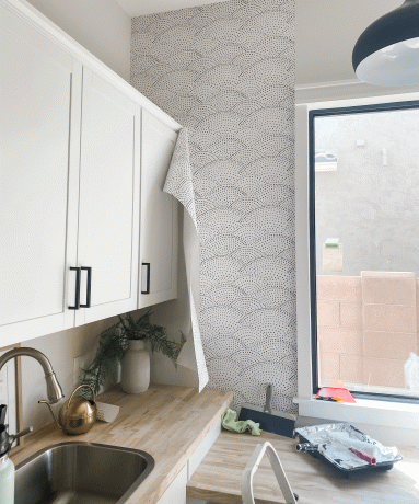 Una cocina con gabinetes blancos con decoración de manijas, revestimiento de papel tapiz blanco y negro con manchas monocromáticas y lámparas redondas modernas