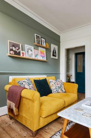 современная гостиная с ярко-зеленой стеной, горчичным диваном и рельсами для картин с художественными репродукциями
