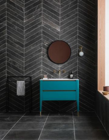 Juodas vonios kambarys su žalsvai mėlyna spintele ir variniu veidrodžiu