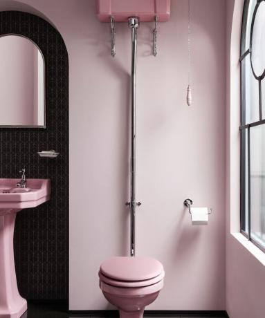 Pinkfarbenes Badezimmerkonzept mit pinkfarbener Toilette, Waschbecken und Wänden und schwarzem Wandkontrast