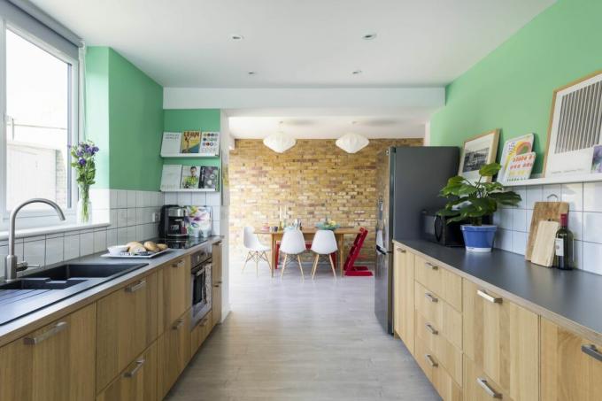 हरे रंग की विशेषता वाली दीवारों और एक ईंट प्रभाव वाली दीवार के साथ उज्ज्वल खुली योजना लकड़ी के रसोई भोजनशाला