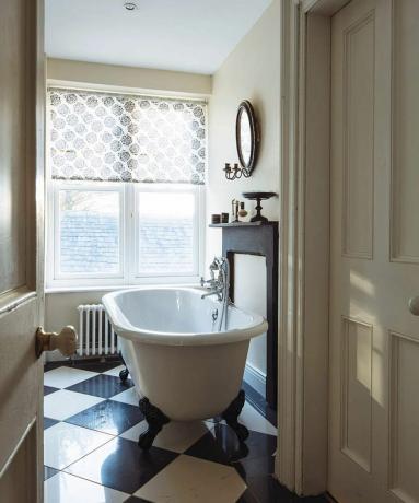 Un bagno color crema con piccola vasca da bagno bianca e pavimento in piastrelle a scacchi bianche e nere