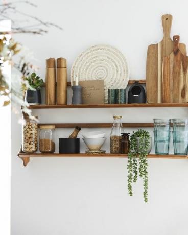 ξύλινα ράφια σε λευκό τοίχο που κρατά φυτά, βάζα και άλλα αξεσουάρ κουζίνας