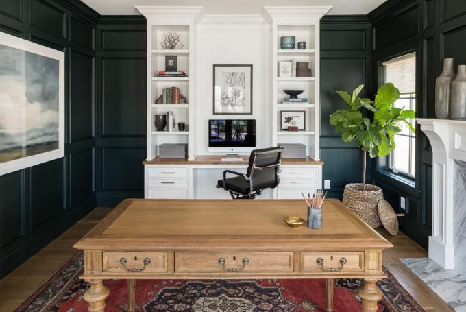Kotitoimisto, jossa on puinen työpöytä, valkoinen kirjahylly ja tummaksi maalattu seinät