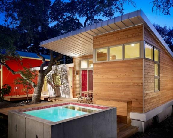 Μια μικρή τσιμεντένια υπέργεια πισίνα δίπλα σε ένα ξύλινο σπίτι και ένα κατάστρωμα