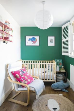 Детска стая със зелена стена, дървен под, килим с мече от юта, дървено легло и фотьойл и играчка кит