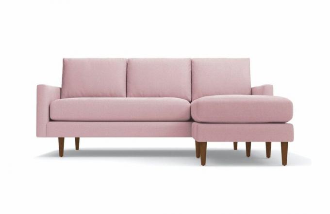 Ένας ροζ βελούδινος τμηματικός καναπές με πόδια από ξύλο πεκάν