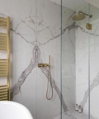 Chuveiro em mármore com portas de vidro transparentes, chuveiro e toalheiro banhados a ouro