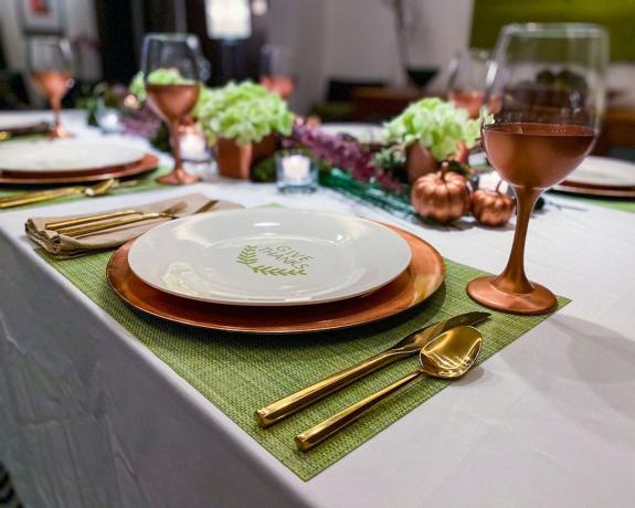Paisaje de mesa de Acción de Gracias con cargadores de cobre, calabazas, copas de vino y centro de mesa