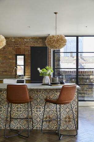 kuhinja u industrijskom stilu s izloženim zidom od opeke, naboranim visećim svjetiljkama, tamnocrvenim barskim stolicama, popločanim šankom za doručak, drvenim podom